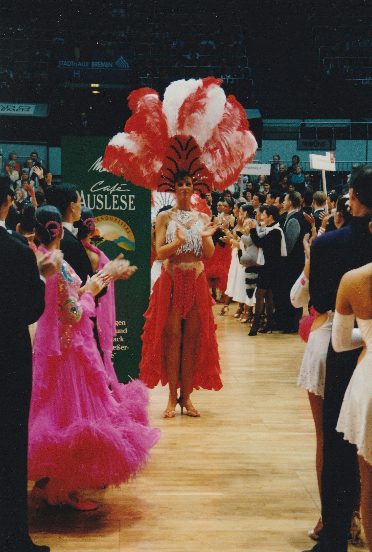 Eine Frau in einem rot-weißen Kleid steht vor einem Schild mit der Aufschrift „Aristose“