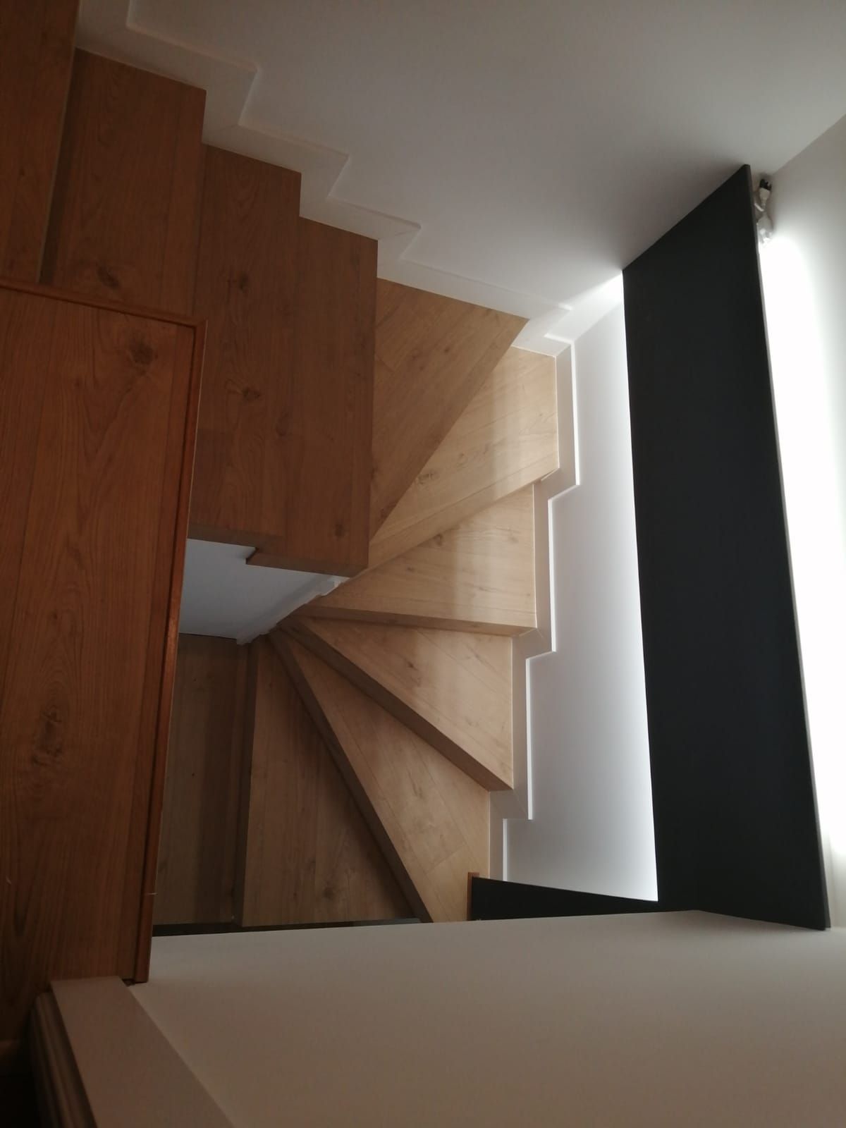 Una escalera de caracol de madera con una pared blanca detrás.