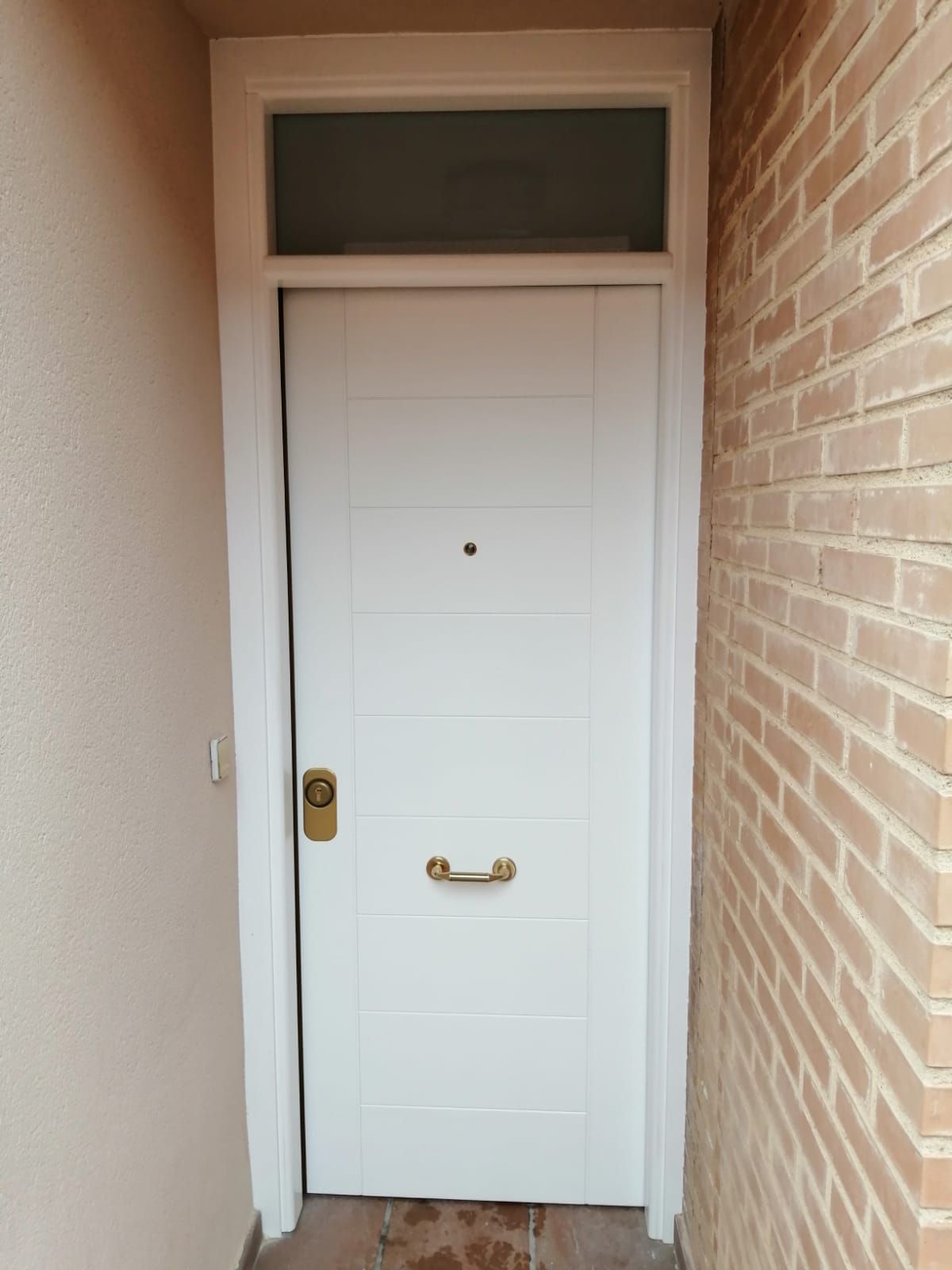 Una puerta blanca está en un pasillo al lado de una pared de ladrillos.