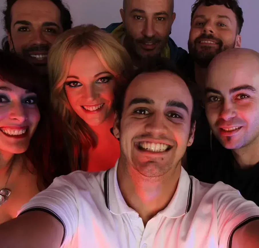 Selfie grupal: siete personas sonriendo a la cámara, iluminadas por luces rojas cálidas y azules frías.