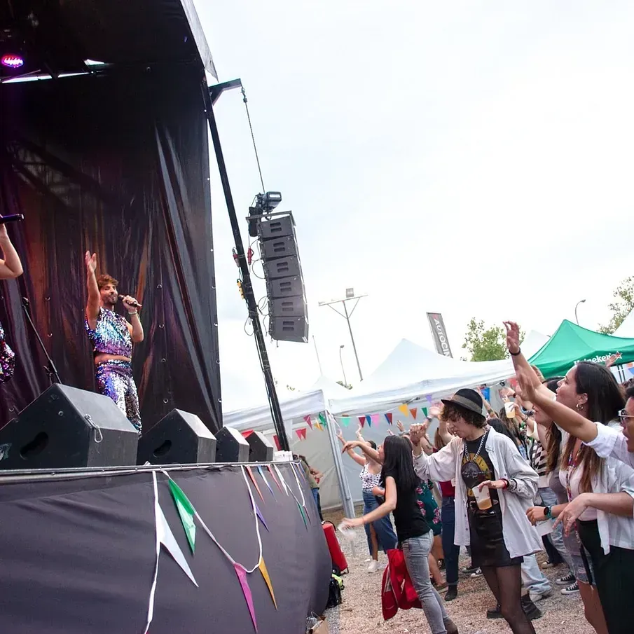 La banda toca en un escenario al aire libre ante una multitud que anima con los brazos en alto.