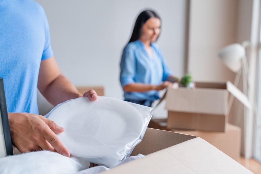 Un hombre sostiene un plato delante de una mujer que está empacando cajas.
