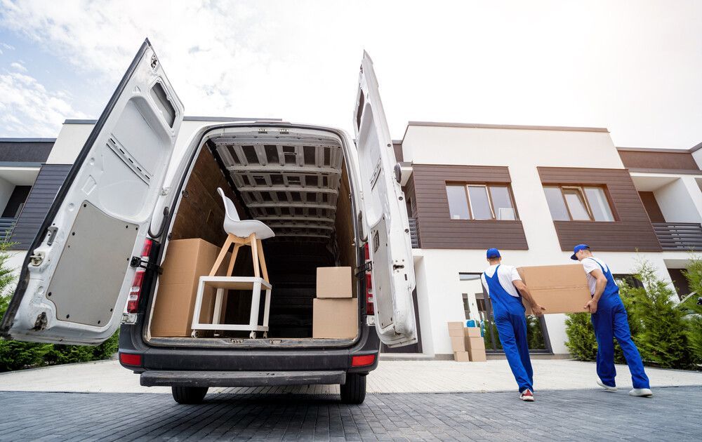 Dos mudadores están cargando cajas en una camioneta frente a una casa.