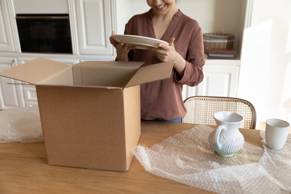 Una mujer sostiene un plato delante de una caja de cartón abierta.