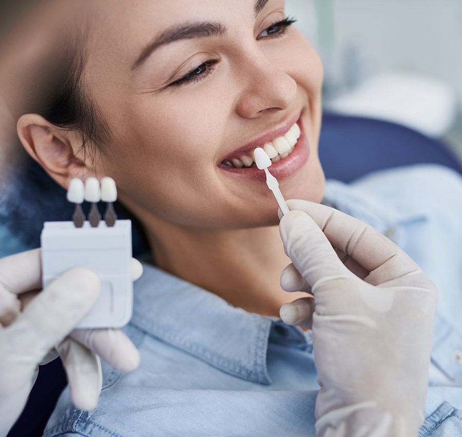 Un dentista aplica gel blanqueador en los dientes de un paciente sonriente durante un procedimiento dental.