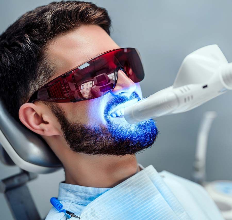 Paciente con protectores oculares rojos recibiendo tratamiento dental con luz azul en una clínica.