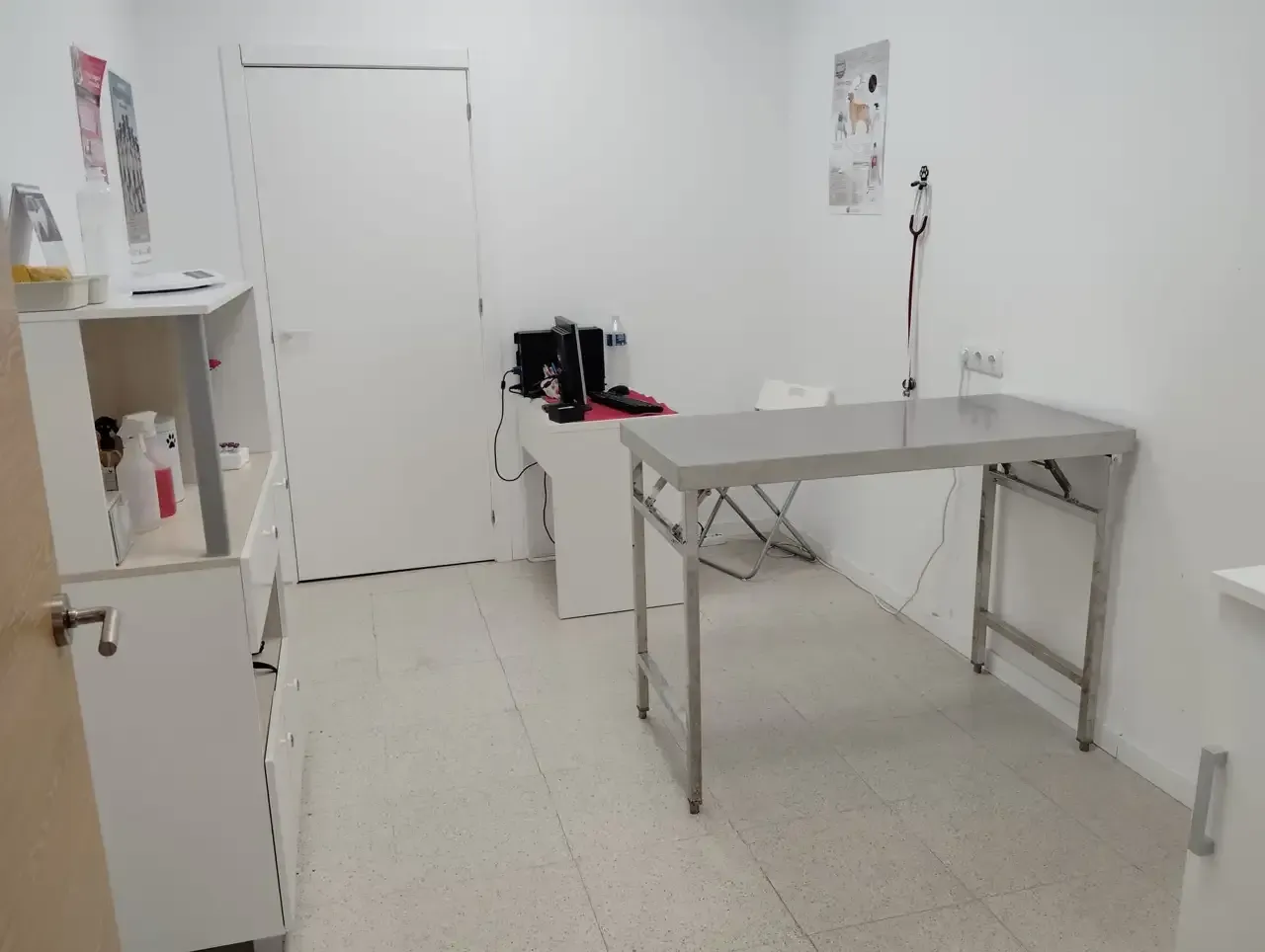 Sala de reconocimiento veterinario: jaula, mesa de trabajo con almohadilla azul, espacio de almacenamiento.