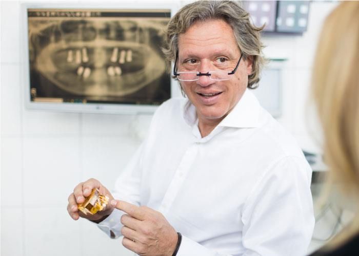 Ein Mann im weißen Hemd zeigt auf ein Zahnmodell