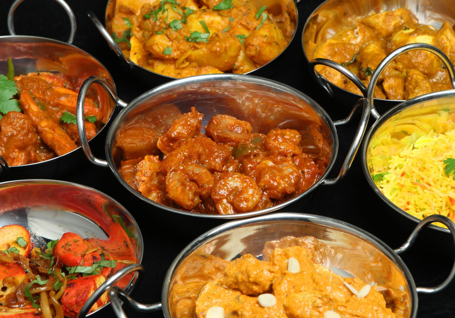 Une sélection de plats indiens (viandes et riz) dans des bols en métal.