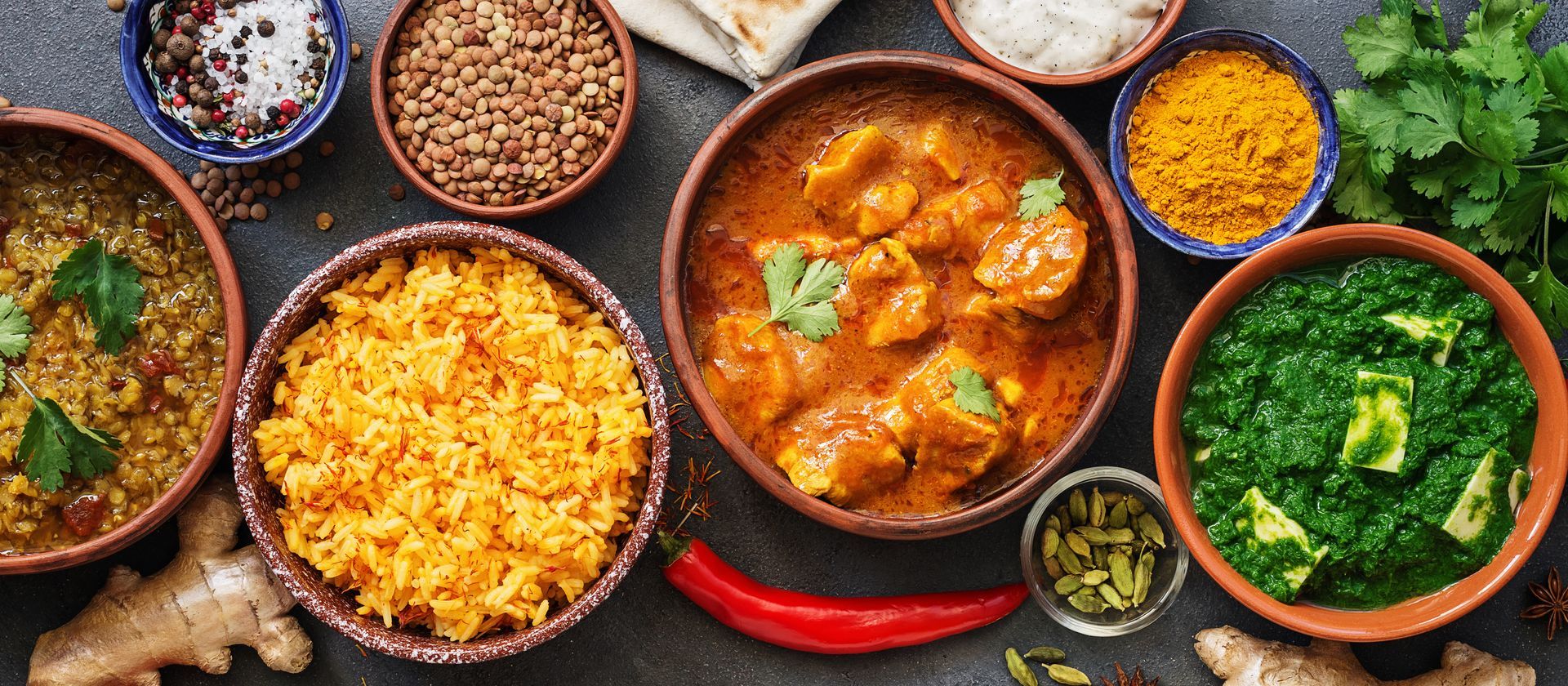 Assortiment de plats indiens colorés dans des bols : riz parfumé, palak paneer, poulet au curry et autres accompagnements.