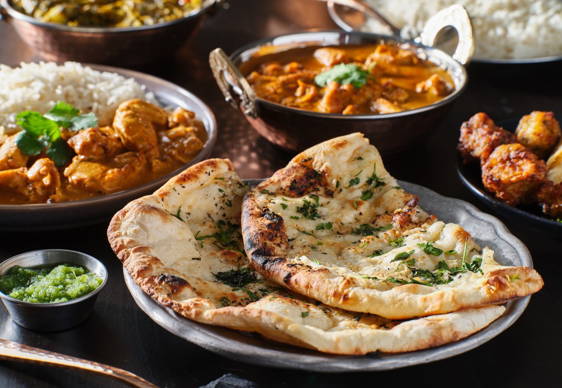 Des plats indiens servis avec des naans garnis de coriandre.