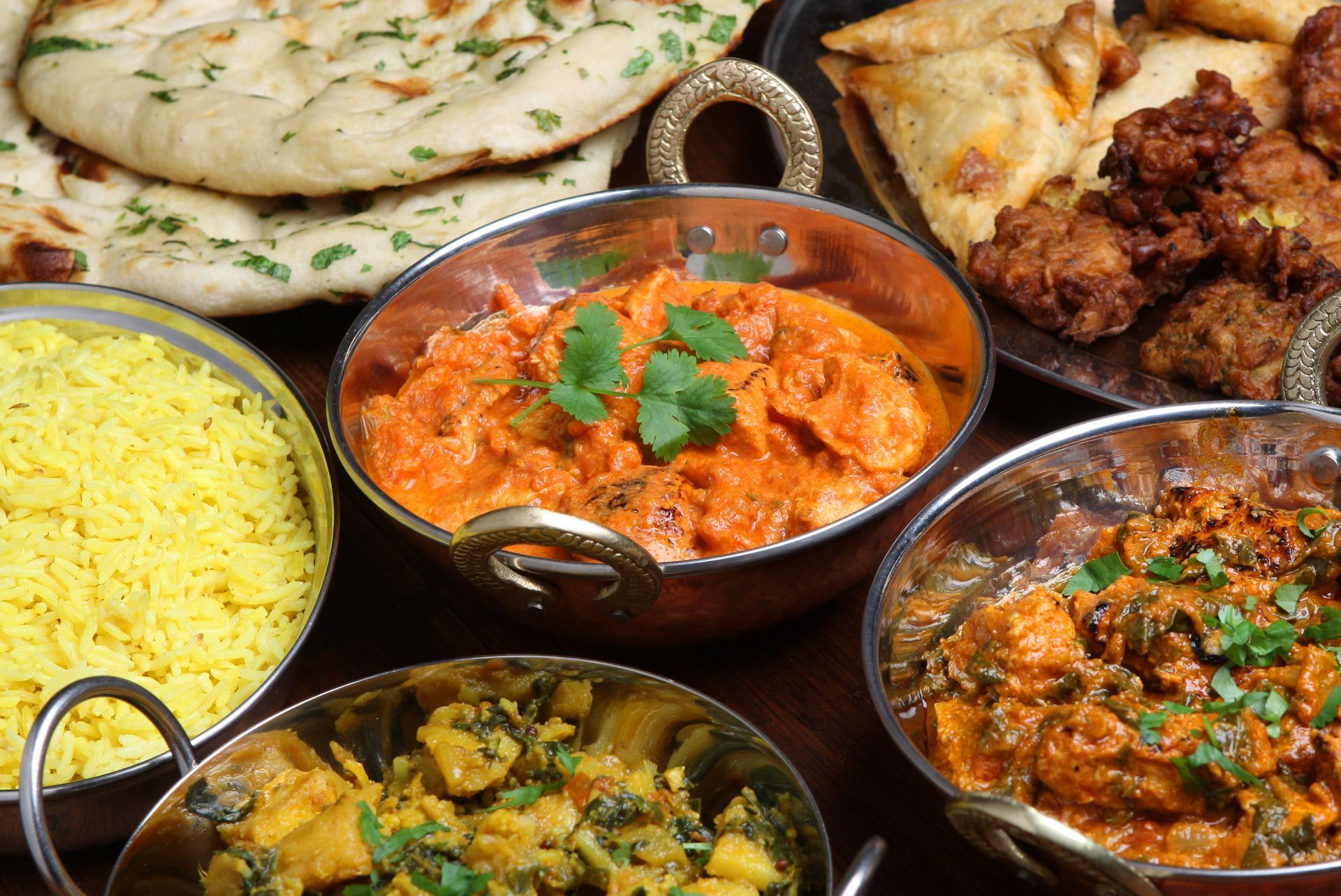 Plusieurs plats indiens à la viande, servis avec du riz et des naans.