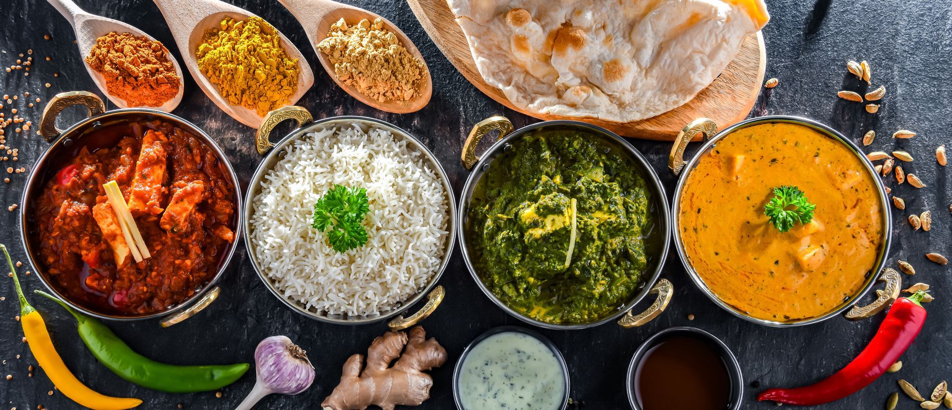 Un assortiment de currys colorés, de chutneys et de pains plats disposés sur une table sombre.