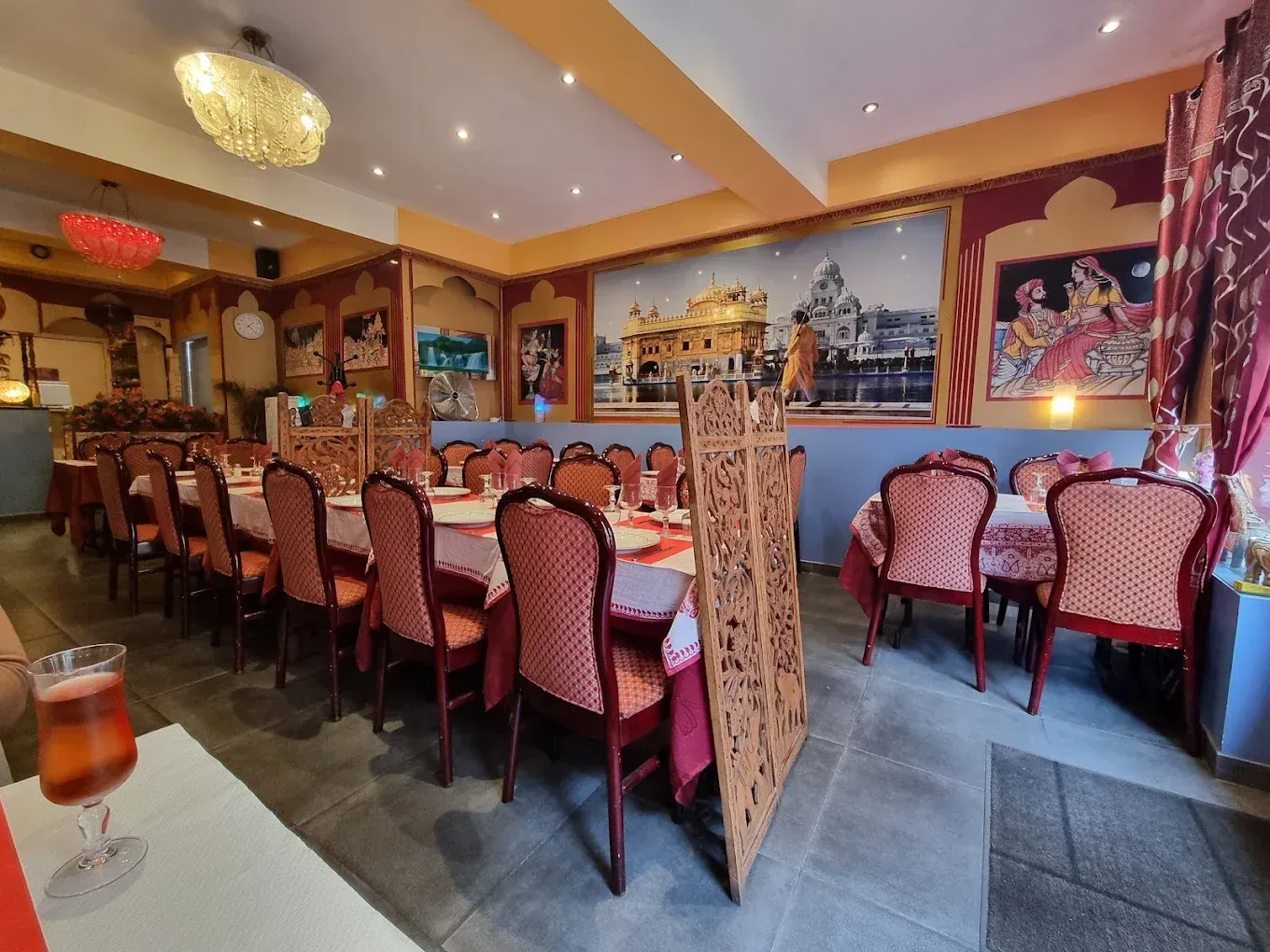 La salle à manger du Taj Mahal Orléans avec des chaises rouges, des tables dressées et un éclairage chaleureux.