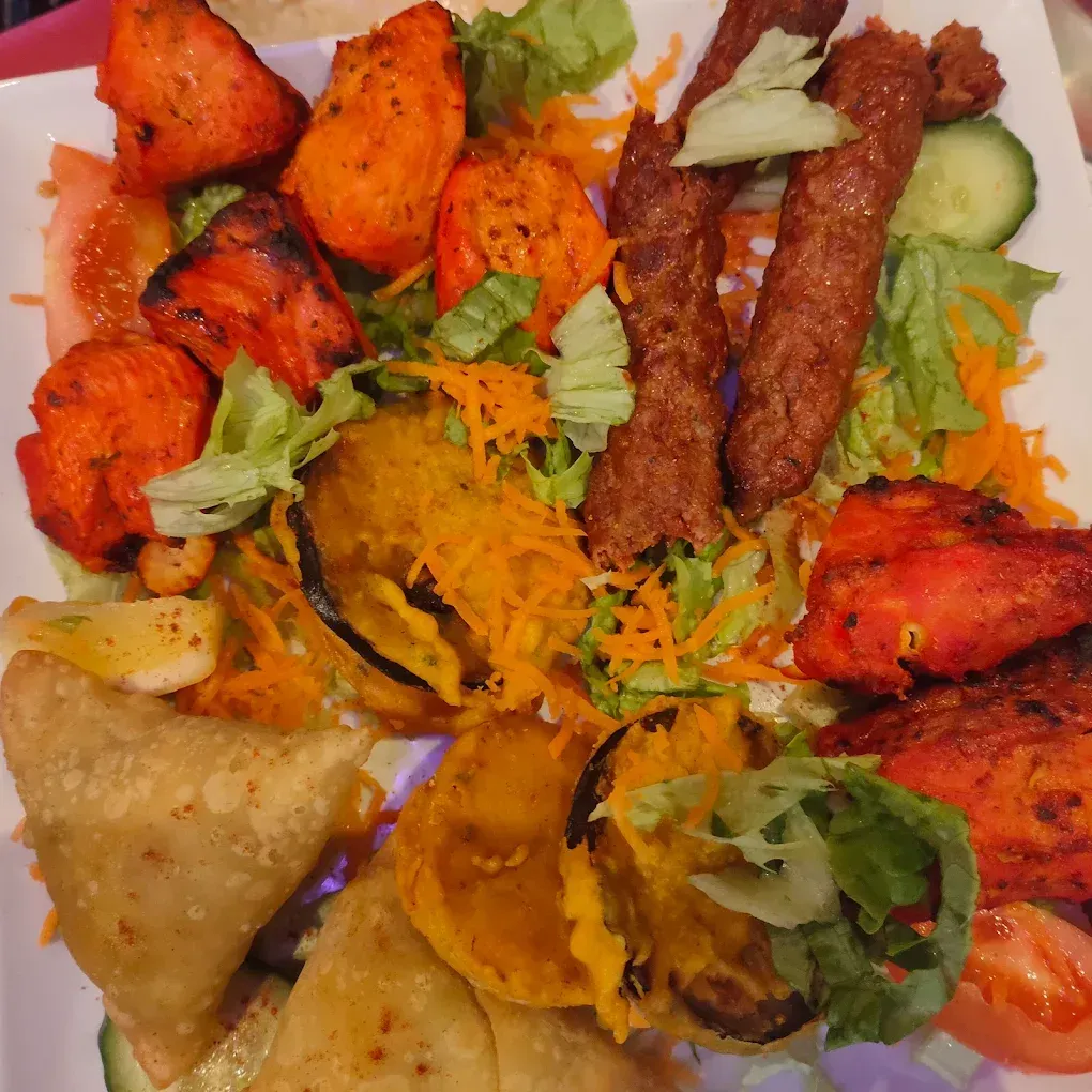 Un assortiment de viandes grillées, de légumes frits et de samosas, servi dans une assiette avec de la salade.