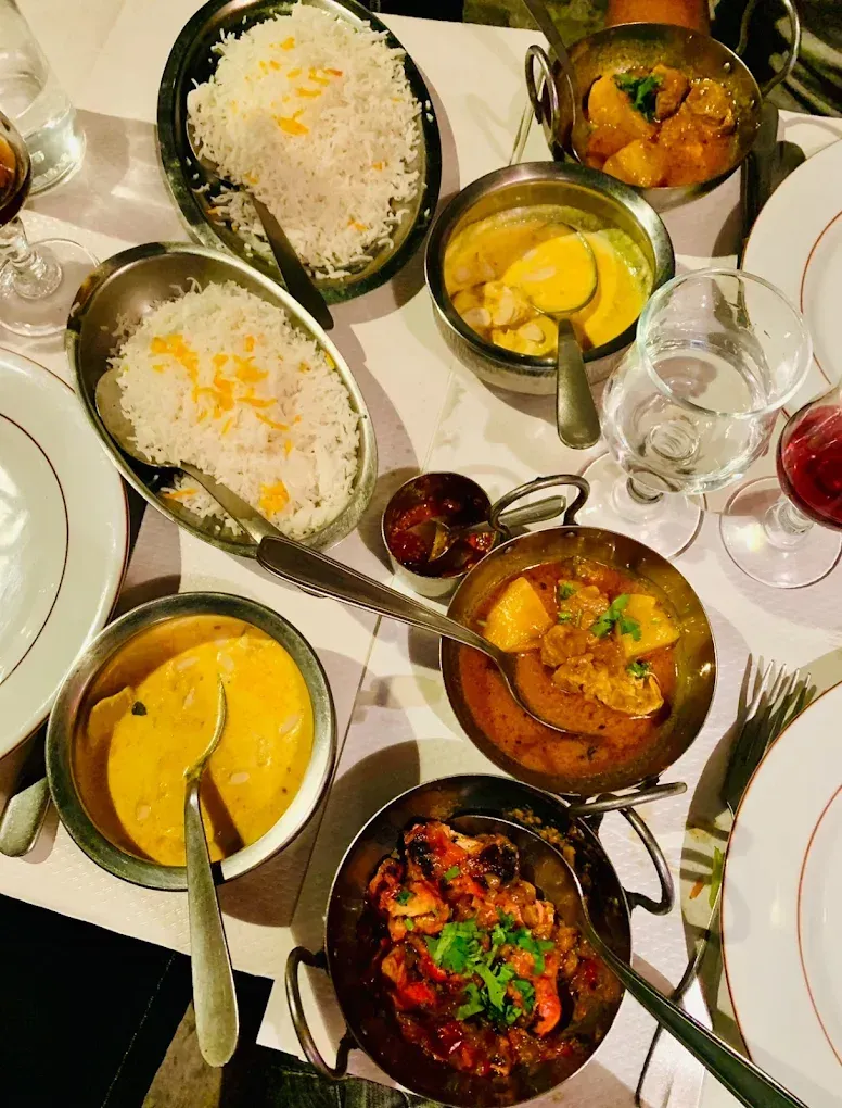 Une table garnie de plusieurs plats de currys indiens, de bols de riz, de naans et de verres à vin.