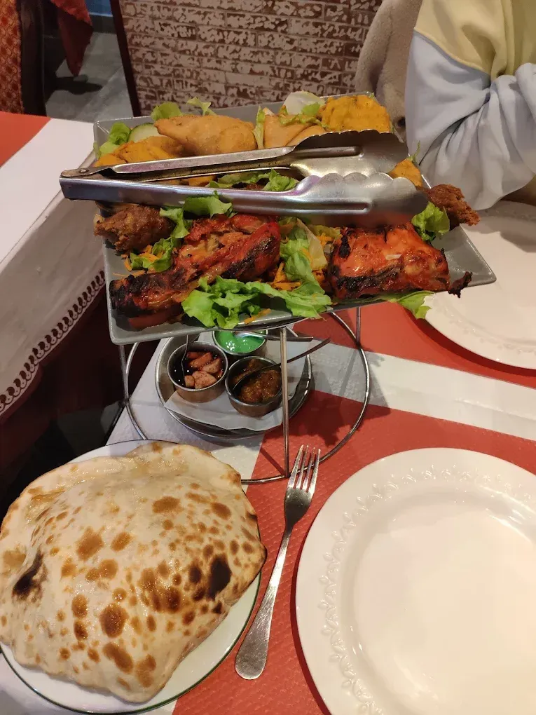 Un plateau de grillades tandoori sur une table de restaurant, avec des pinces et des petits pots à condiments à proximité.