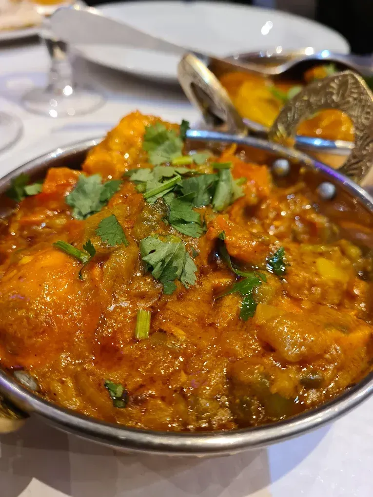Un plat de viande en sauce dans un bol en métal, garni de coriandre.