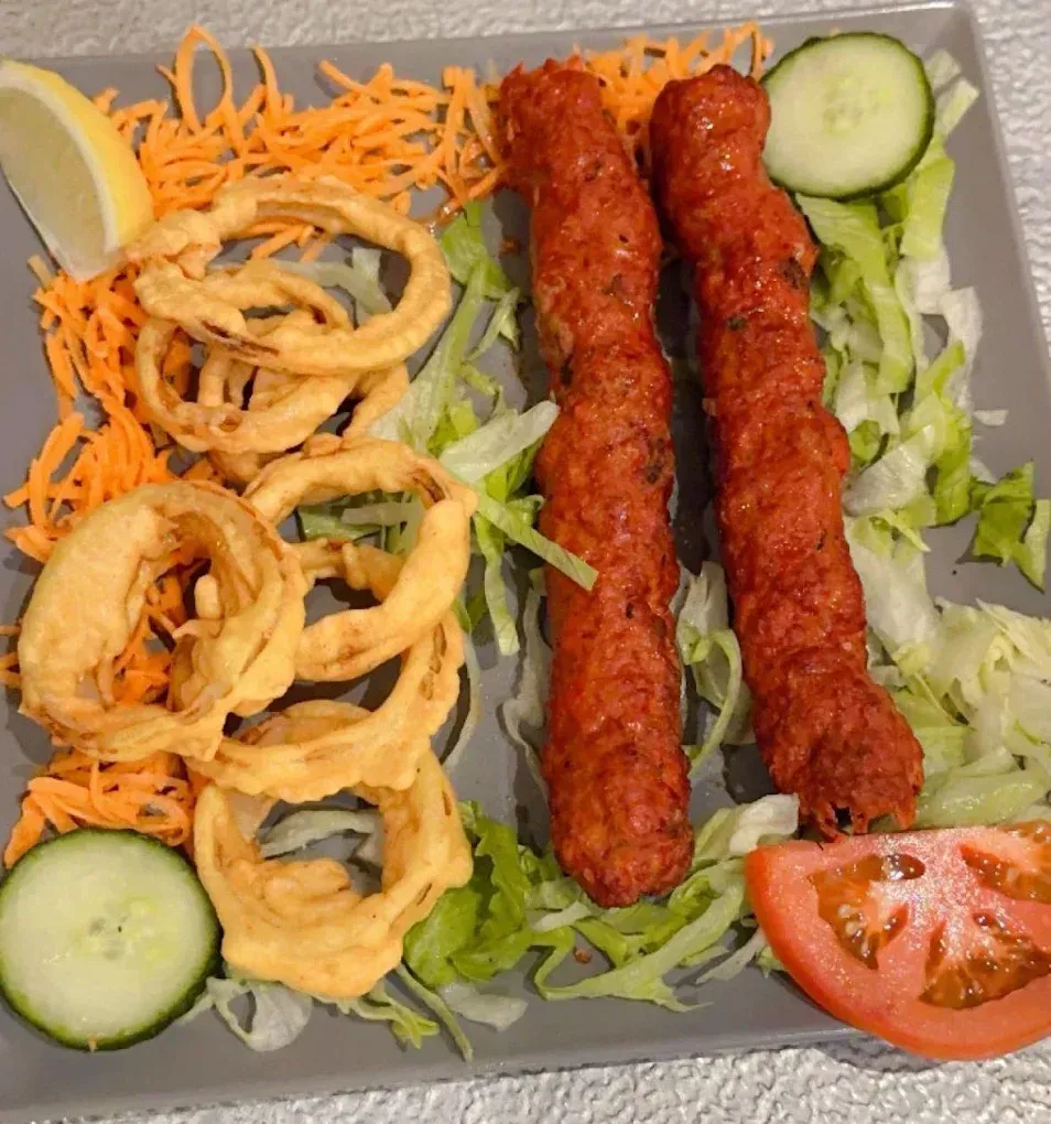 Des brochettes grillées, des rondelles d'oignon frites et une salade, servies sur un plateau.