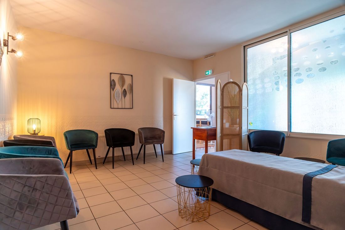 Salle d'attente avec chaises, table de massage et table d'appoint près d'une grande fenêtre.