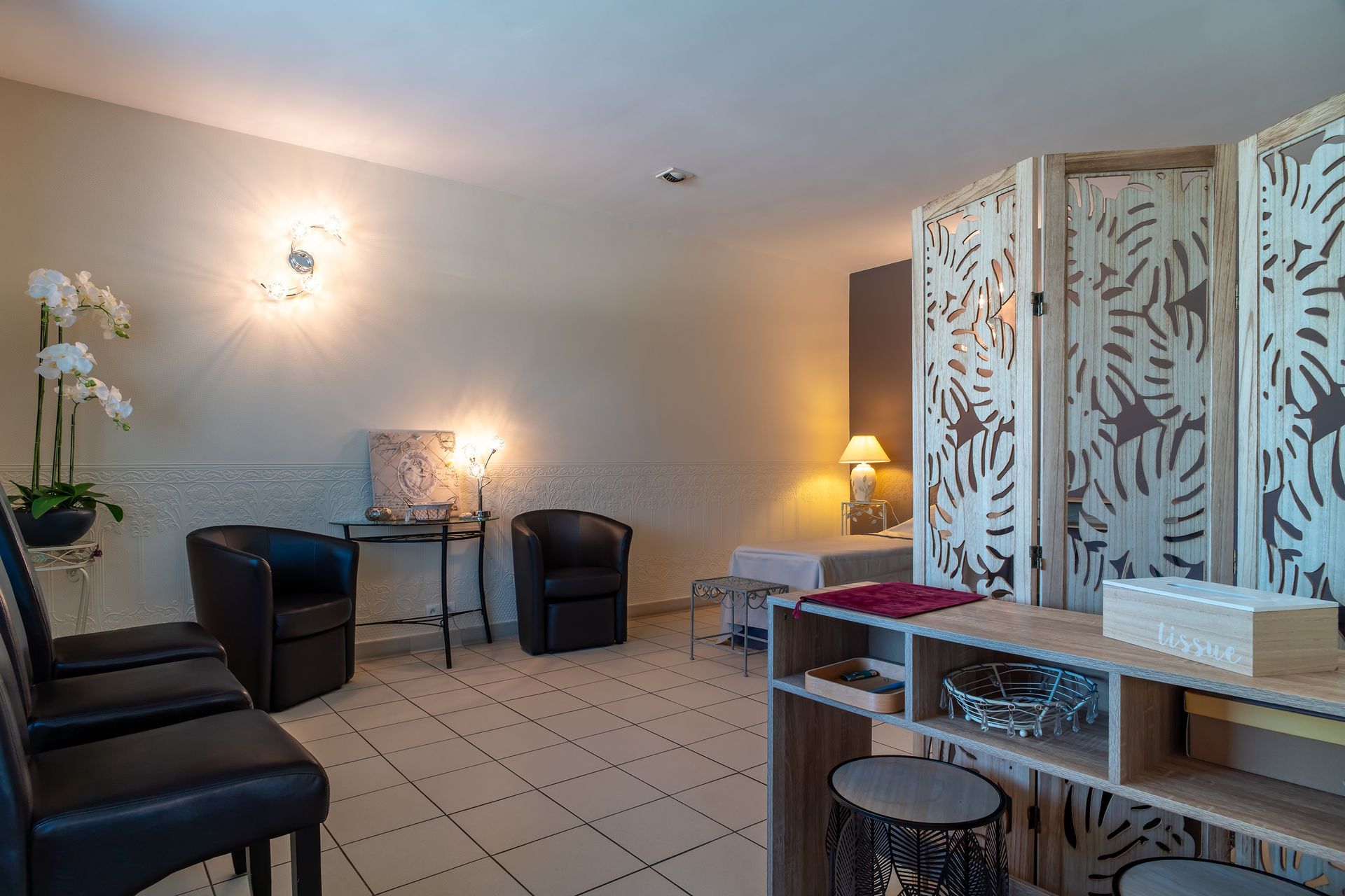 Salle d'attente avec chaises noires, orchidées et paravent décoratif.