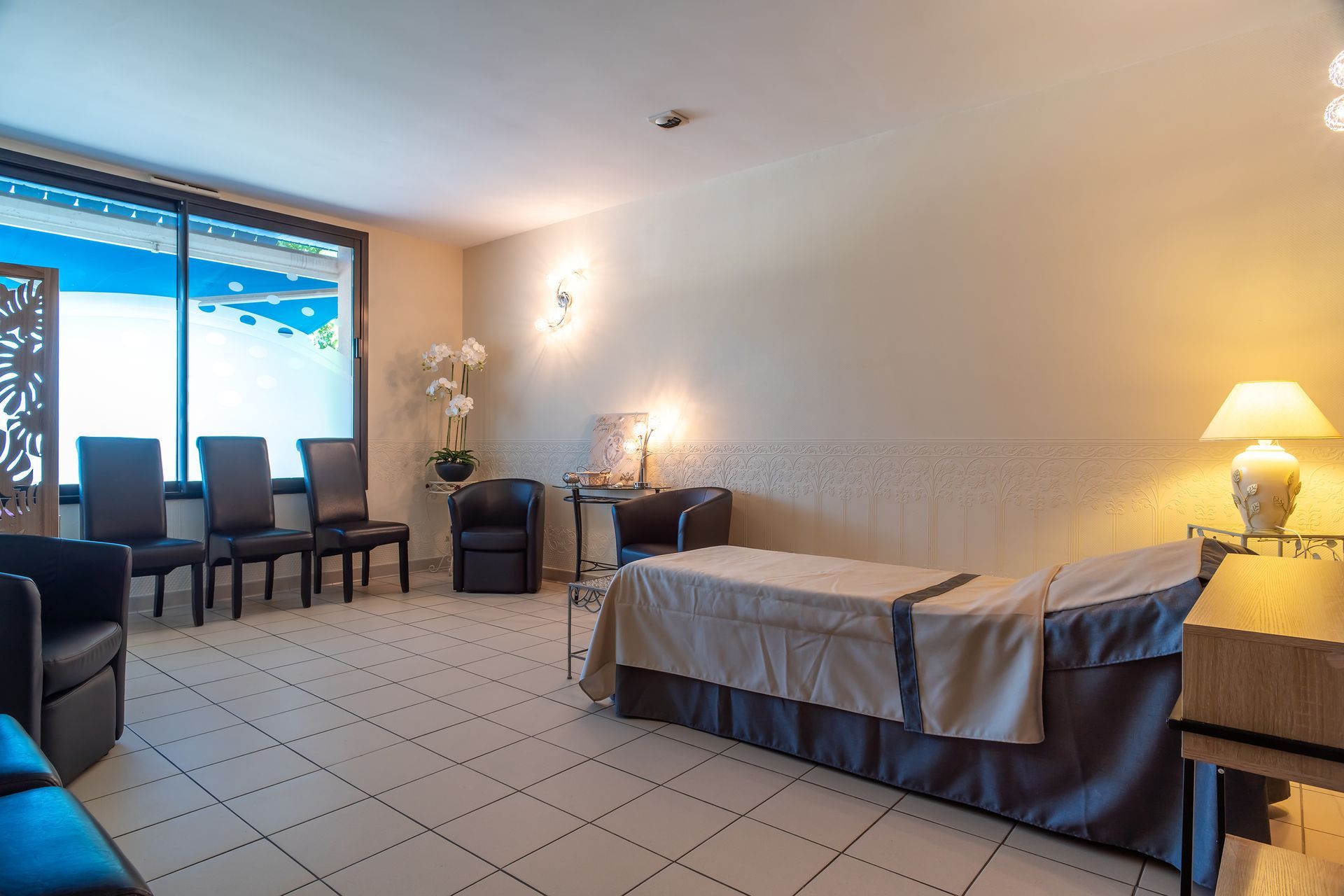 Une chambre lumineuse avec des chaises, un lit et une fenêtre donnant sur un ciel bleu.