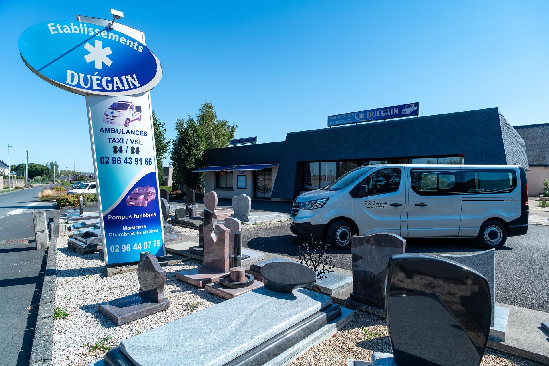Une devanture de maison funéraire avec des pierres tombales exposées à l'extérieur et une camionnette blanche.