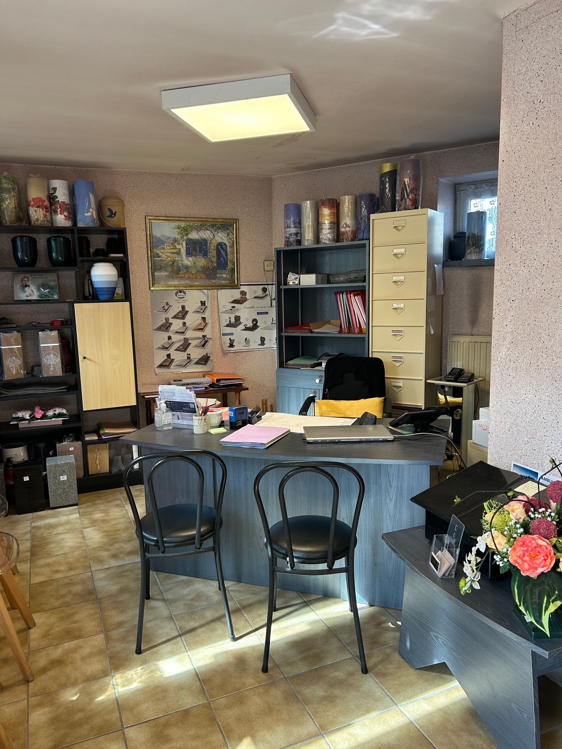Intérieur d'un bureau avec un bureau, des chaises et des étagères. Un bouquet de fleurs est posé sur un banc.