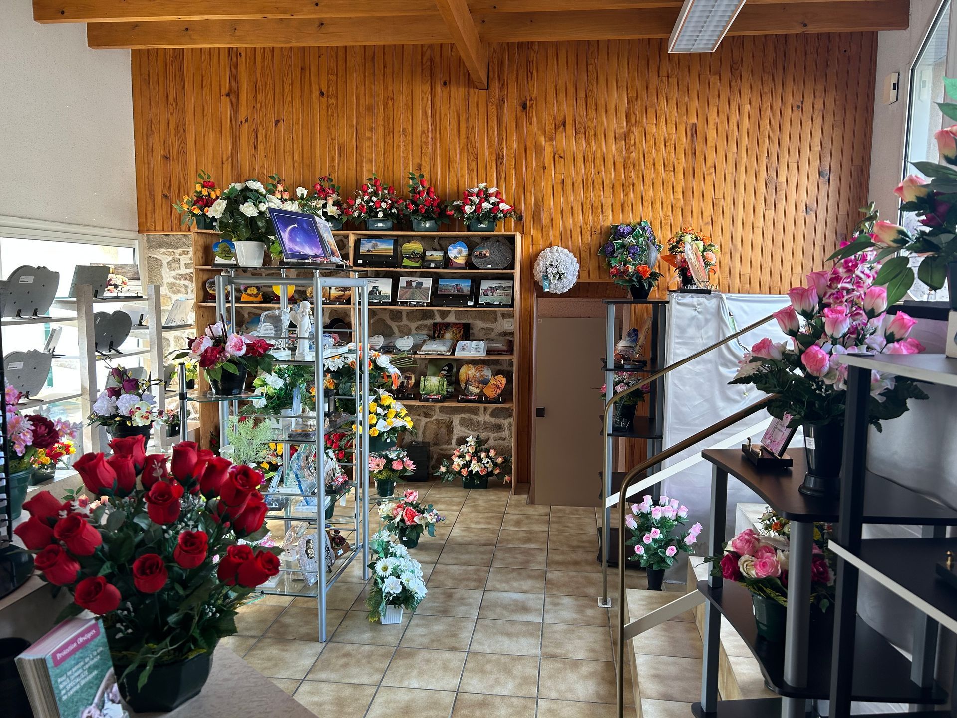 Intérieur d'un magasin de fleurs avec diverses compositions et présentations florales, un mur en bois marron et des étagères avec des urnes.