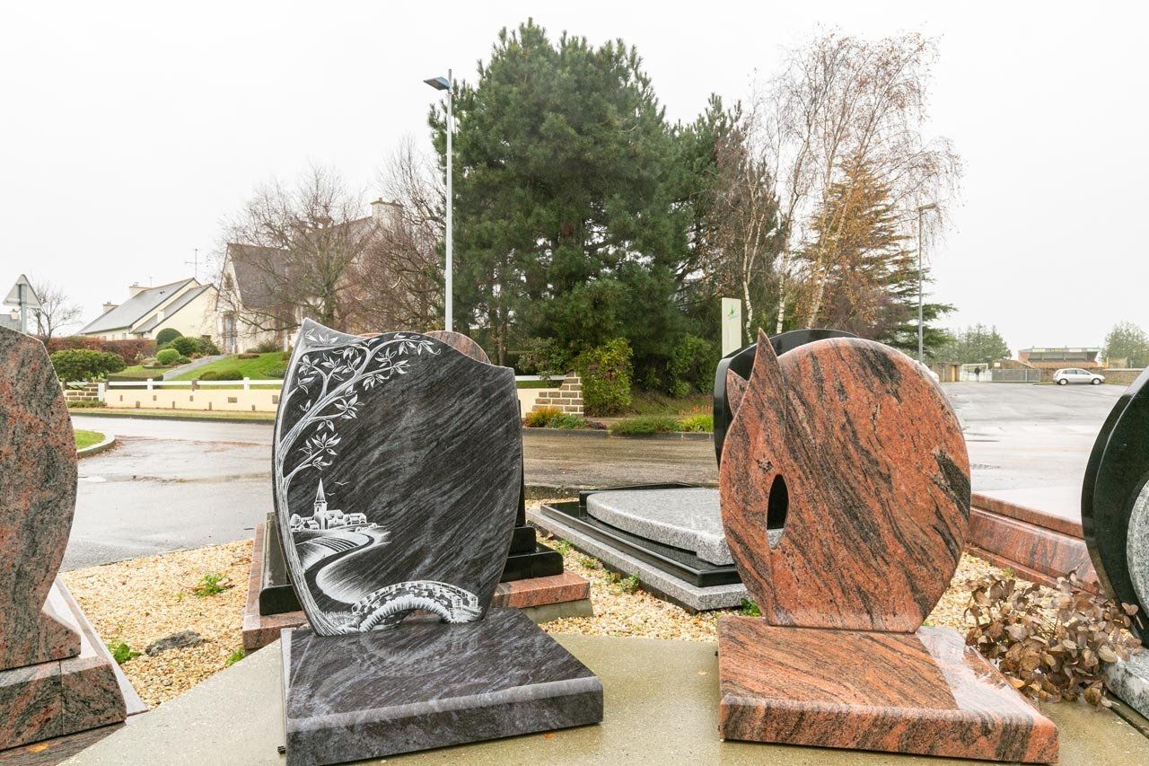 Pierres tombales d'exposition. Granit foncé et marbre rouge, certains ornés de gravures, sont exposés en extérieur.