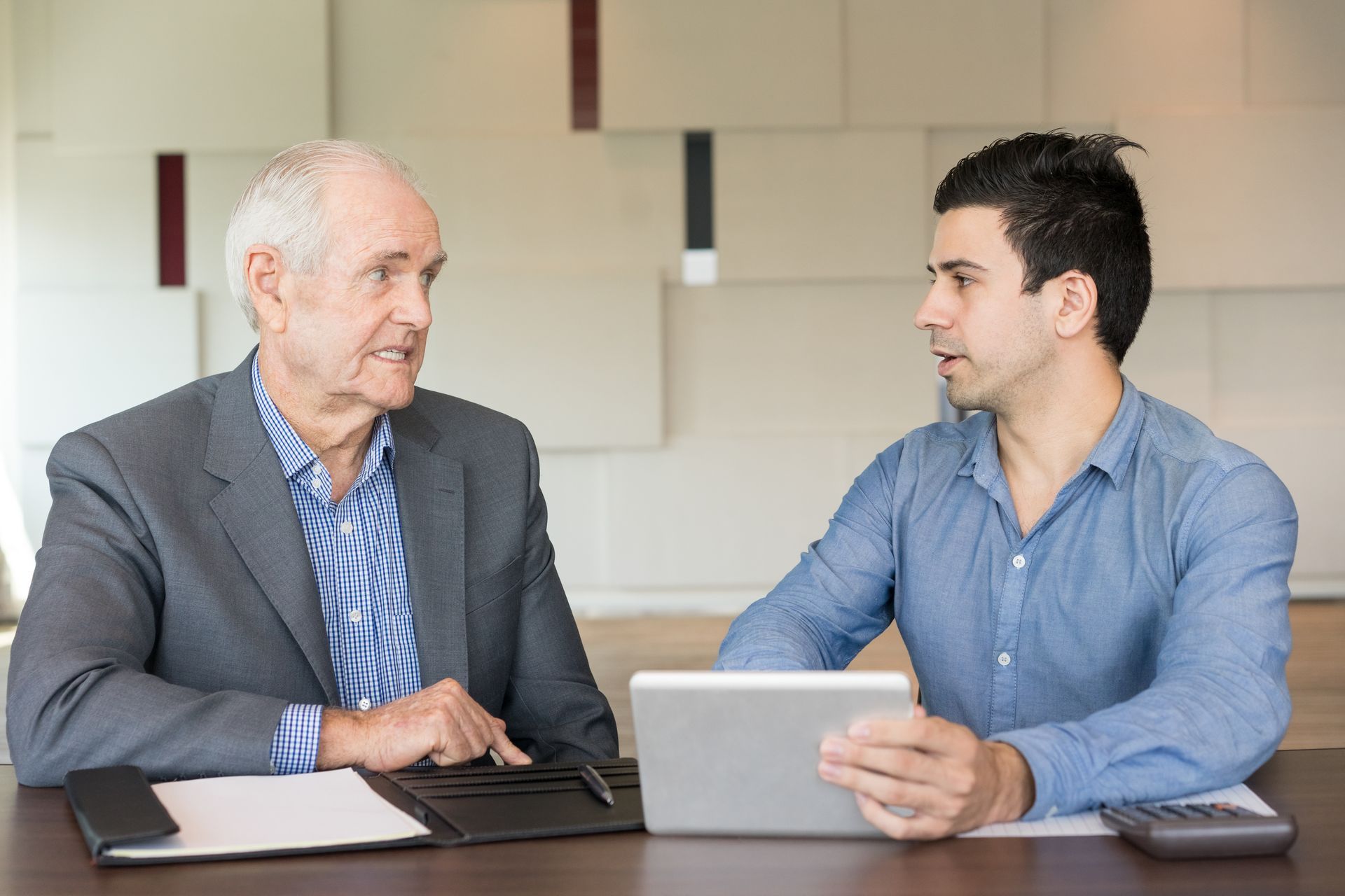 Un homme plus âgé et un homme plus jeune à une table, discutant de documents et d'une tablette.