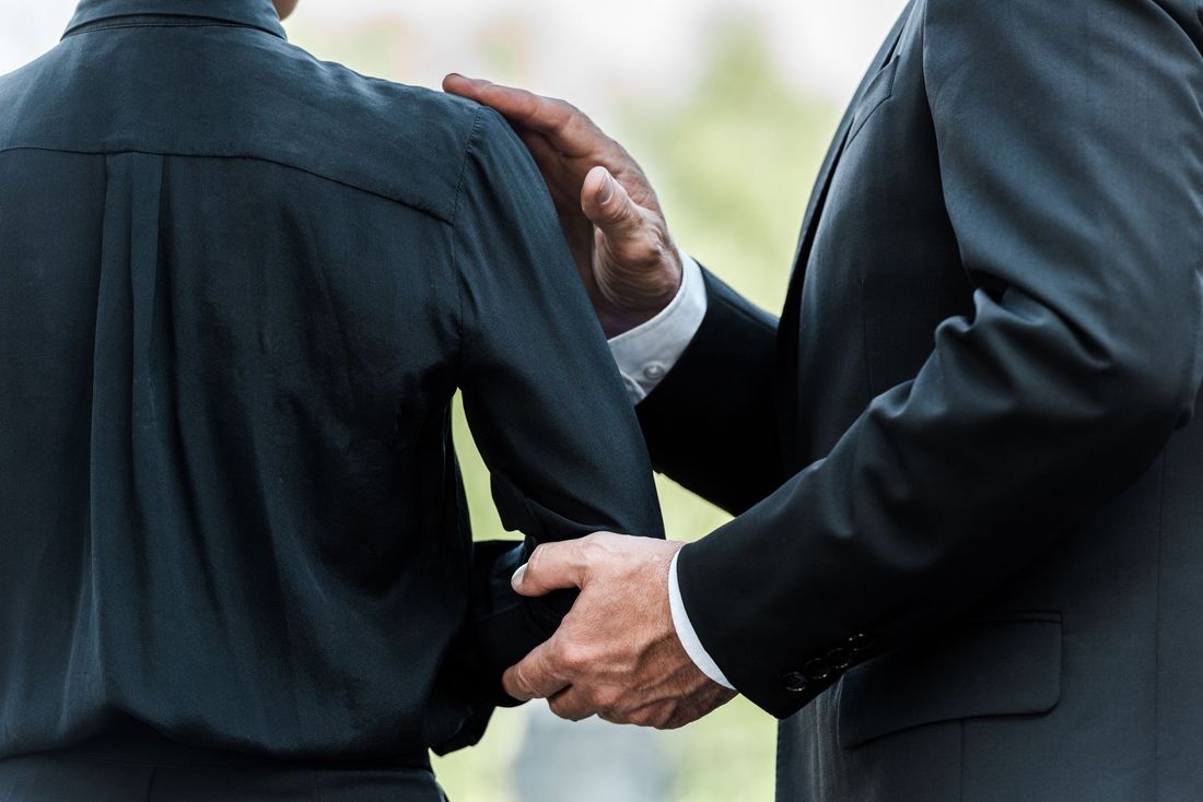 Un homme en costume pose une main réconfortante sur l'épaule d'une personne vêtue de noir.