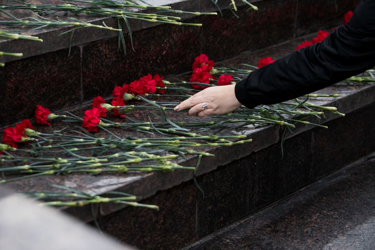 Une personne dépose des œillets rouges sur les marches d'un mémorial.