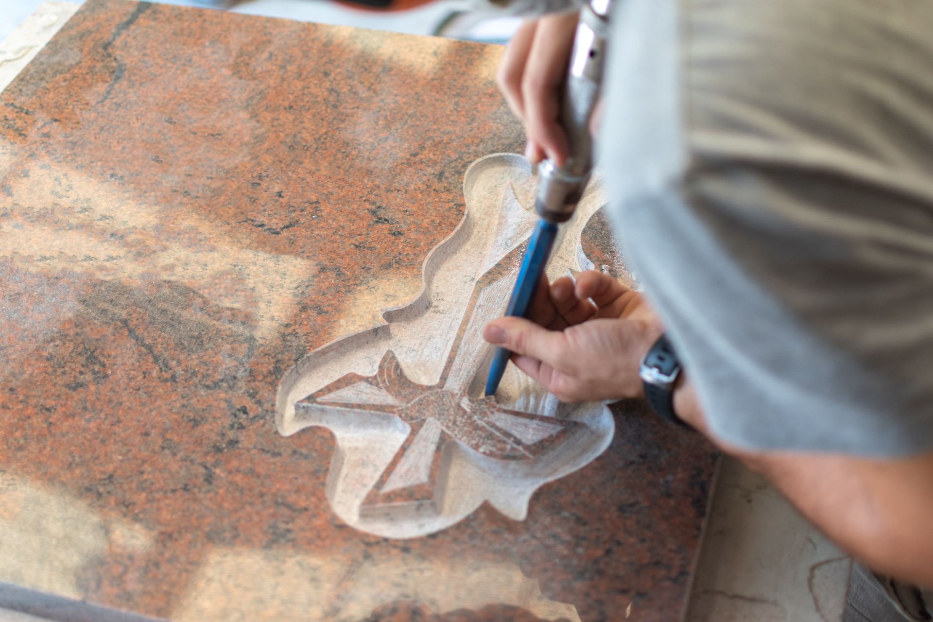 Personne utilisant un outil électrique pour sculpter un motif détaillé dans une grande pierre brun rougeâtre.