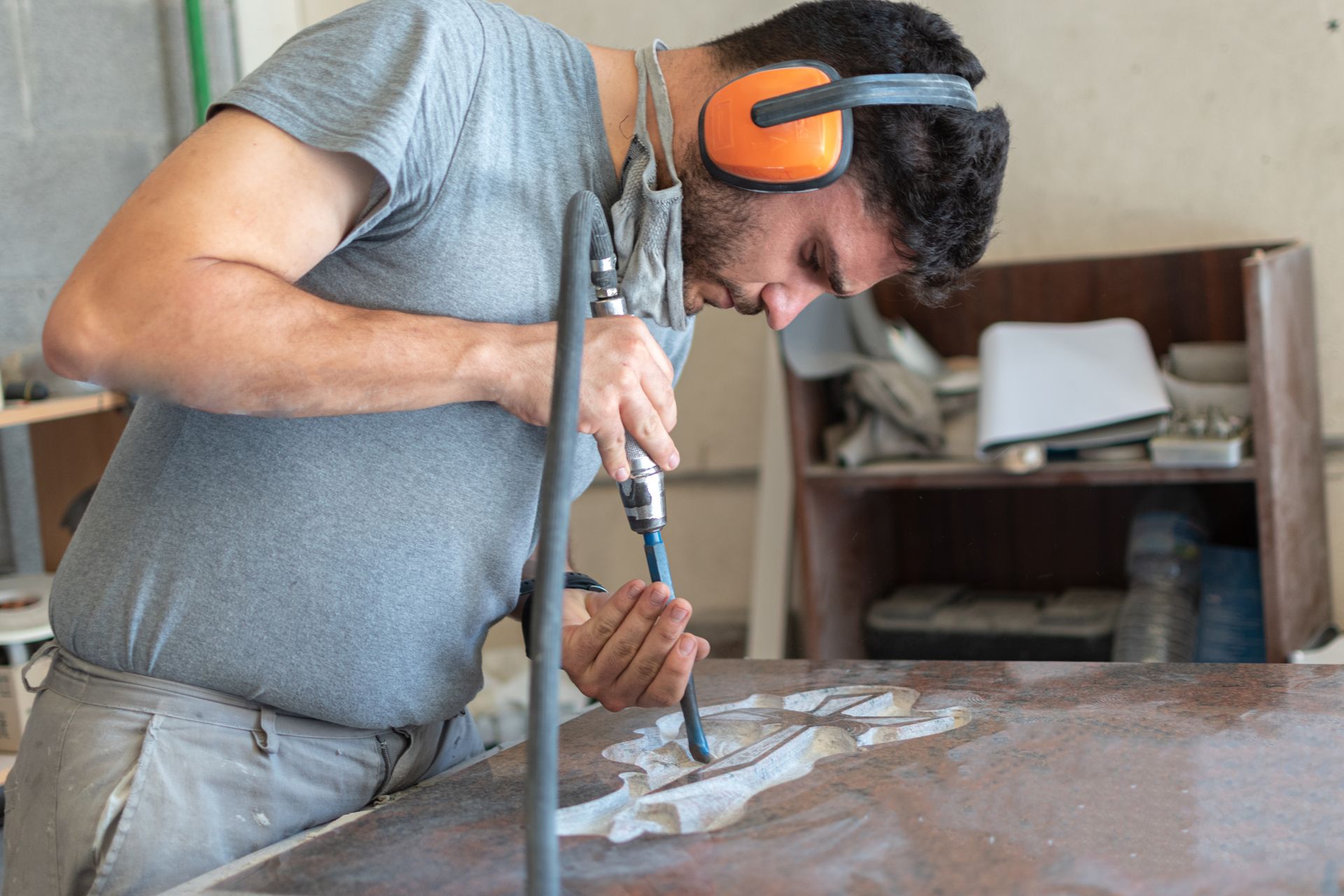 Un homme portant une protection auditive utilise un outil pour travailler sur une surface de couleur foncée dans un atelier.