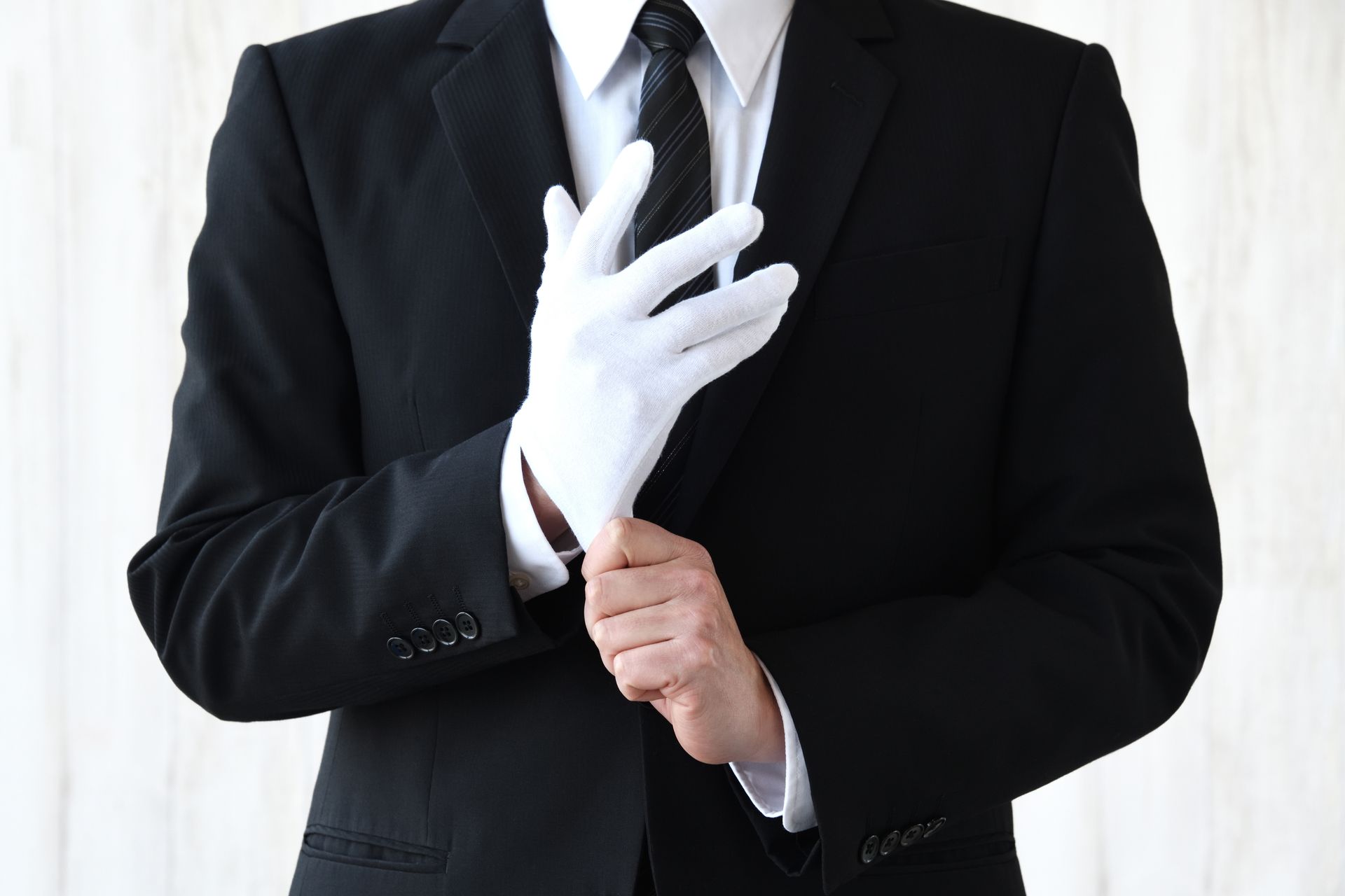 Personne en costume noir ajustant un gant blanc.