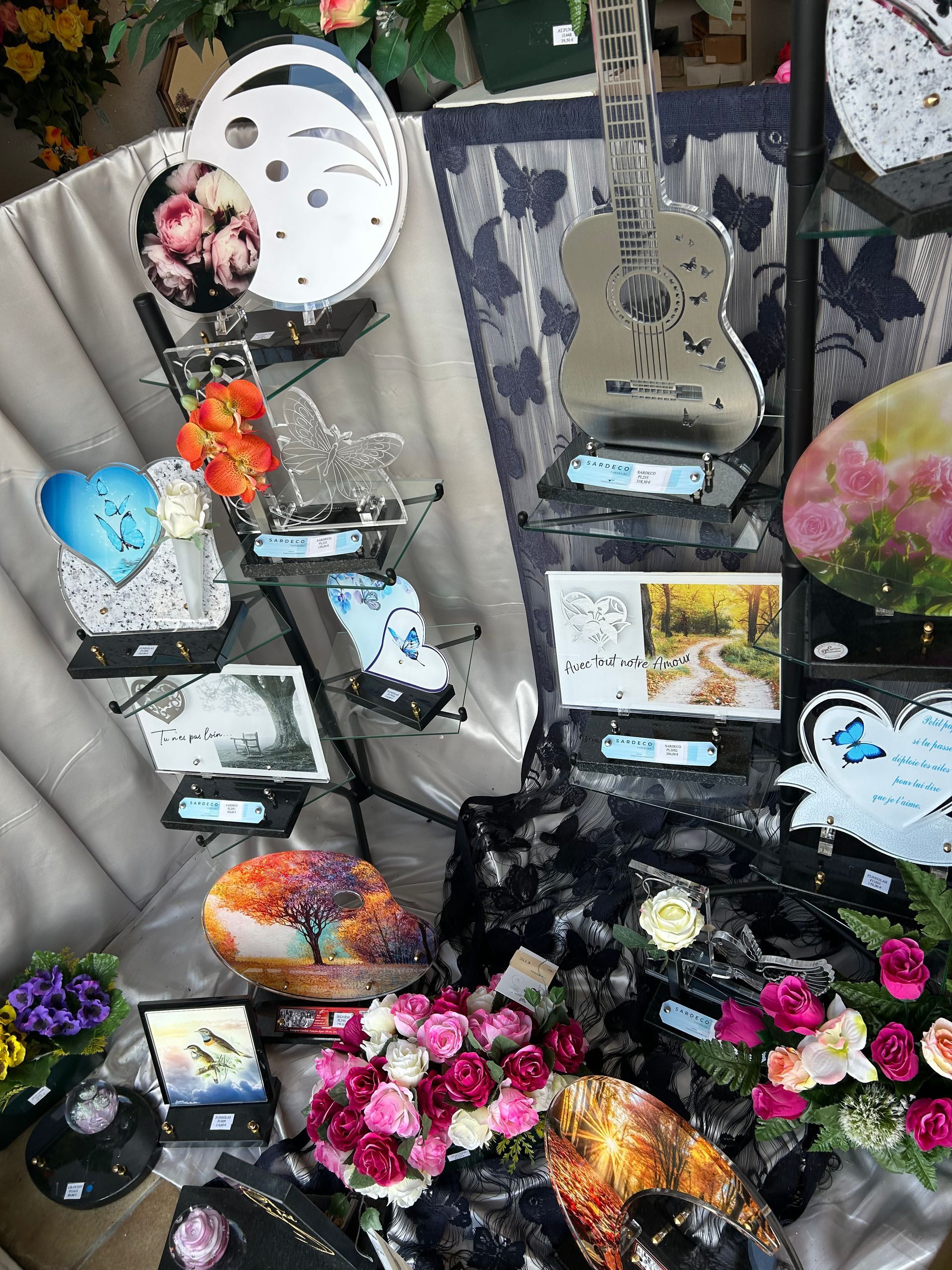 Exposition de plaques commémoratives, dont une en forme de guitare, avec des fleurs dans une boutique.