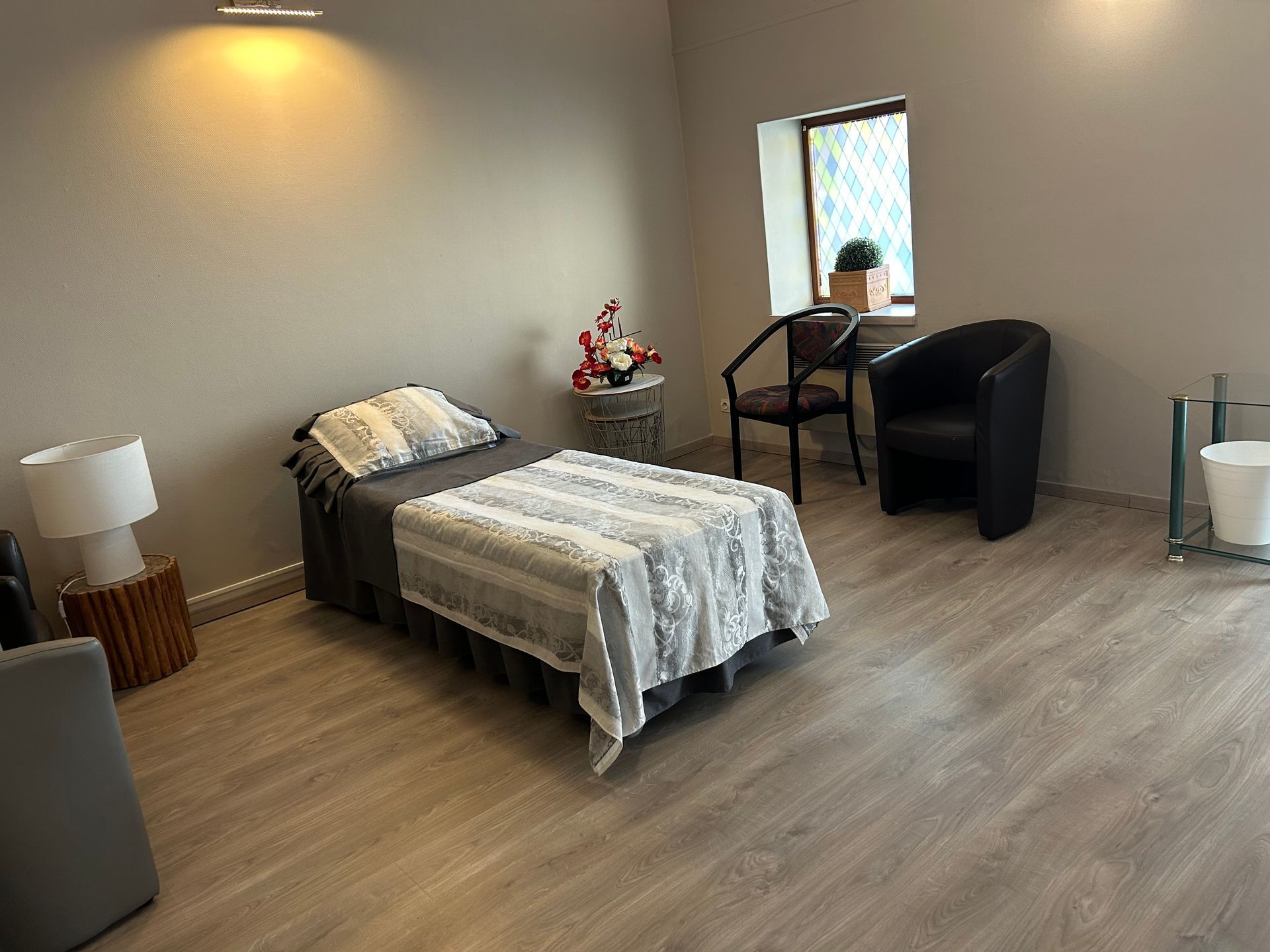 Chambre funéraire avec un lit, deux fauteuils, une lampe et des fleurs.