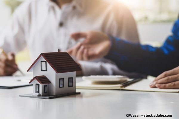 Steuerbüro Christl – Zwei Personen sitzen am Schreibtisch mit einem Modellhaus