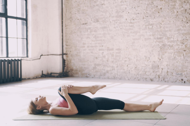Una mujer está acostada boca abajo sobre una esterilla de yoga en una habitación.