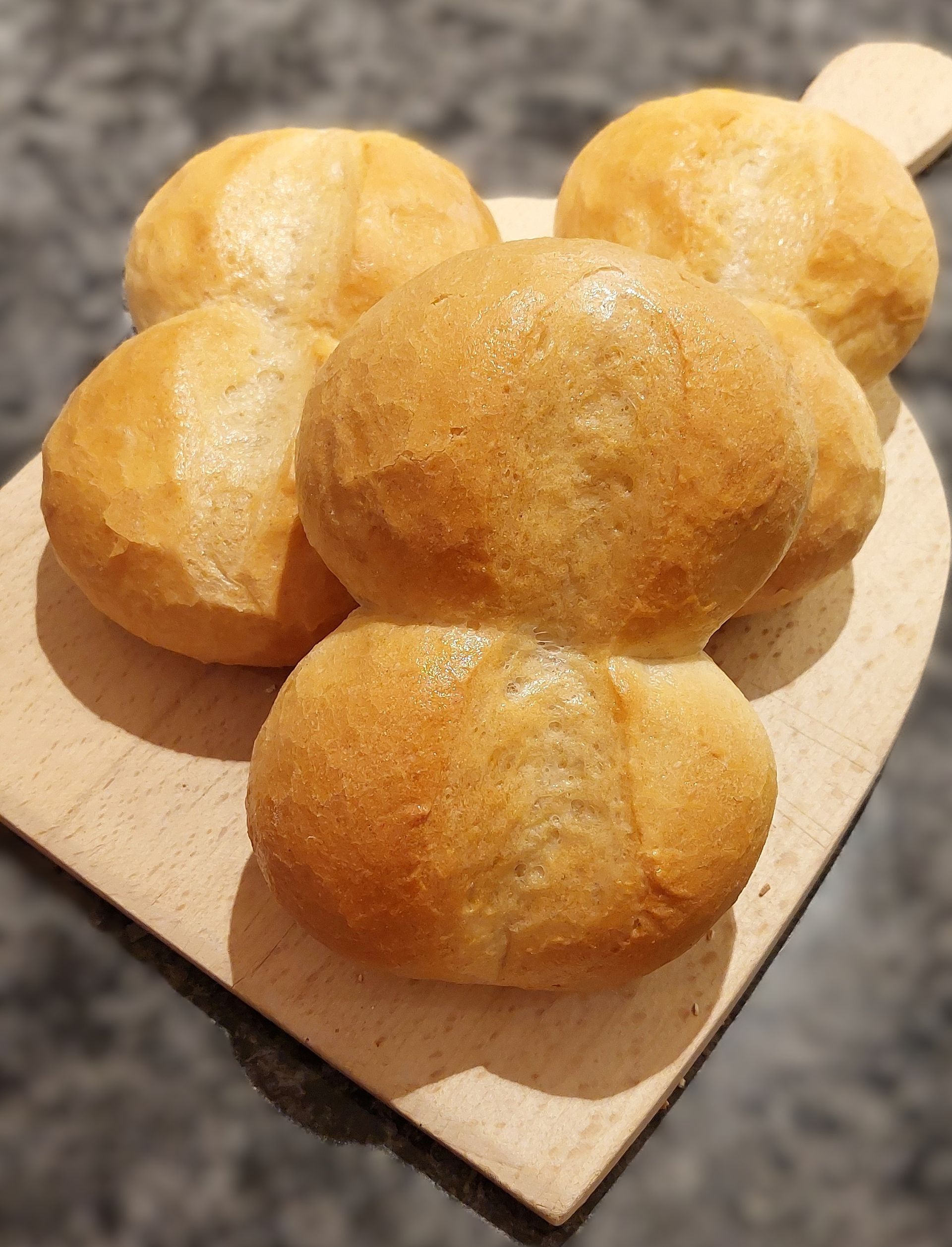 Vier frische Schnittbrötchen auf einem Holzblech