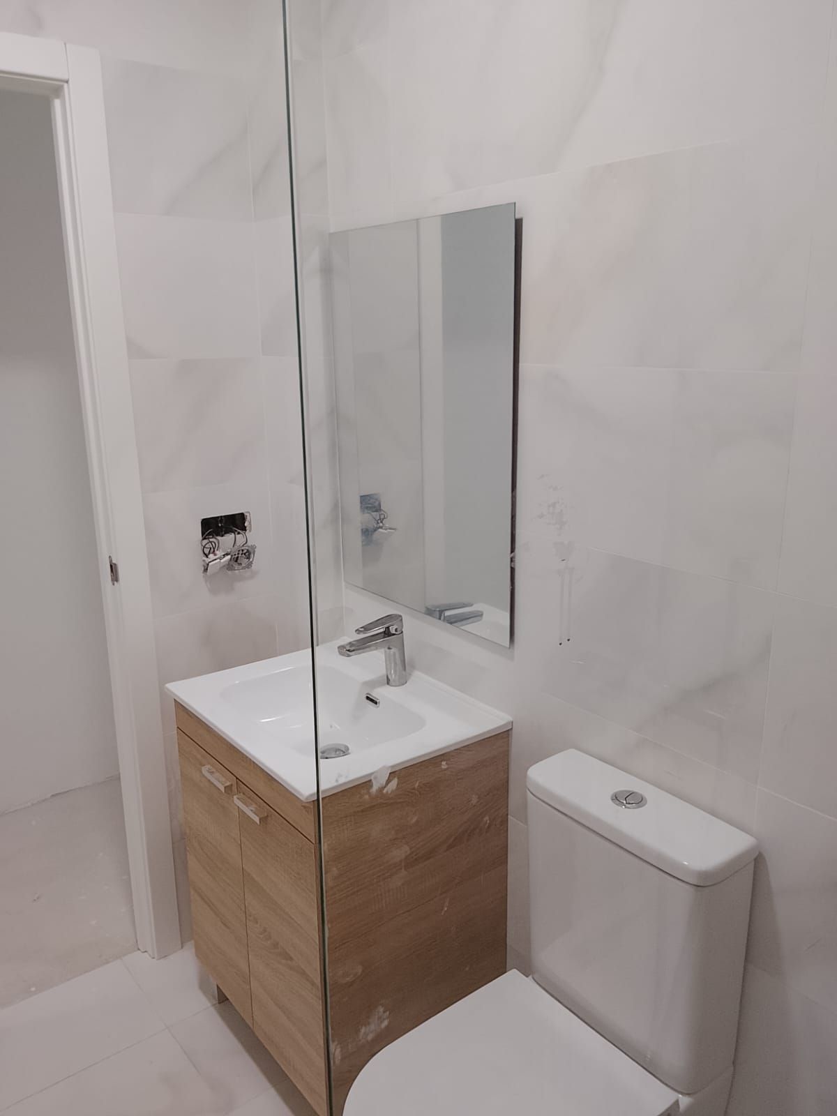 Baño moderno con azulejos blancos, mueble de lavabo de madera, espejo e inodoro.