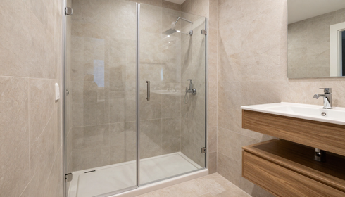 Baño moderno en tonos beige, con mampara de ducha de cristal y mueble de lavabo de madera.