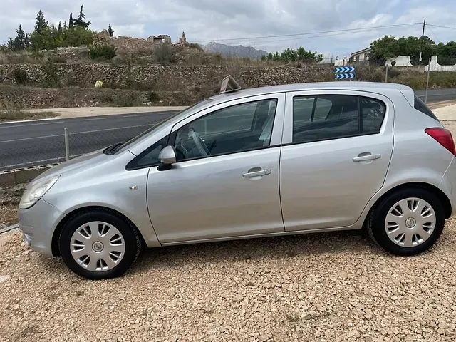 Un coche plateado está aparcado en un terreno de grava al lado de una carretera.