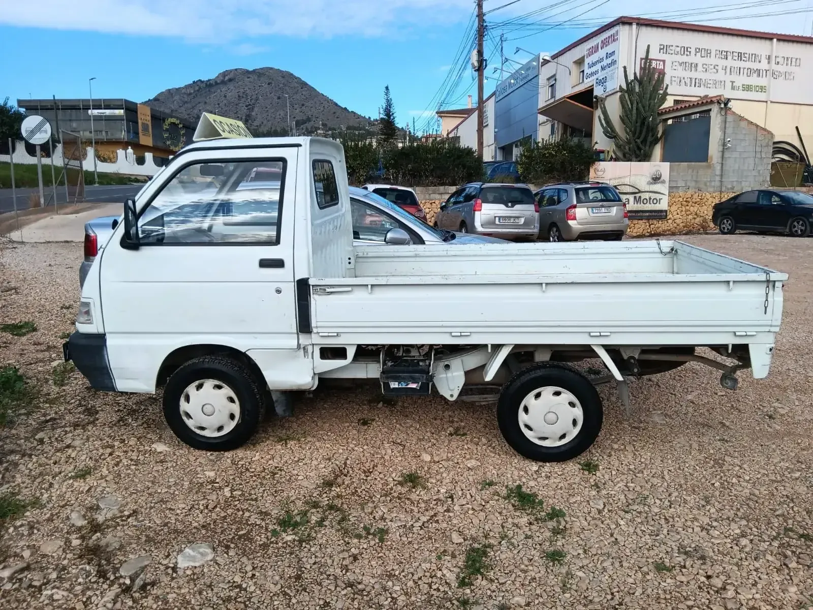 Un camión blanco está estacionado en un lote de grava frente a un edificio.