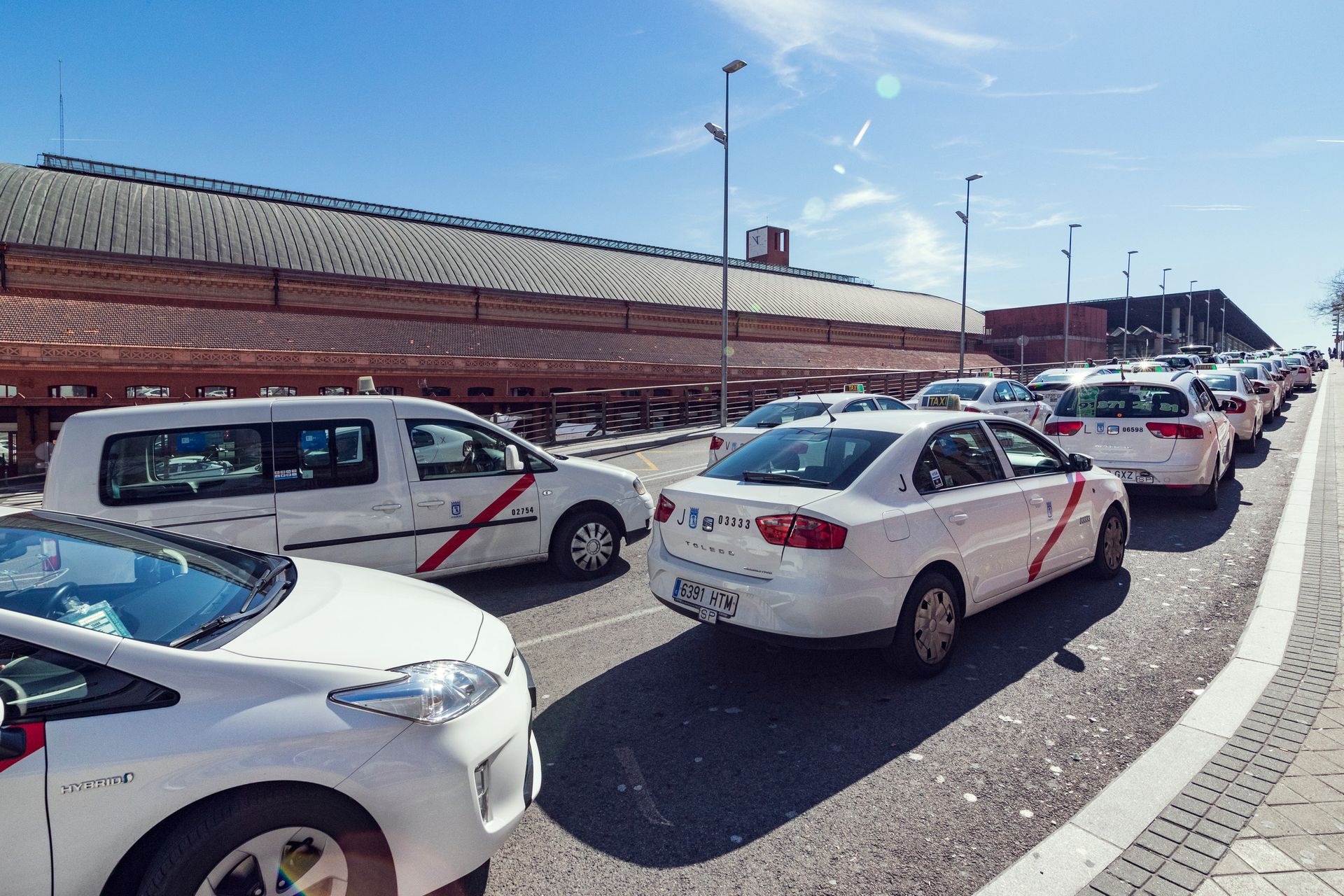 Taxis alineados en una calle frente a un edificio de ladrillo en un día soleado.