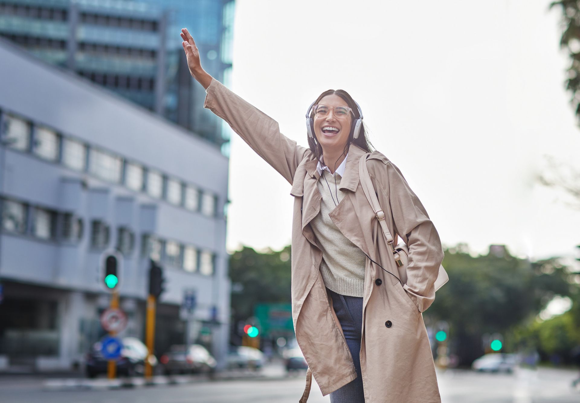 Mujer tomando un taxi en una calle de la ciudad, con auriculares, sonriendo y agitando el brazo.