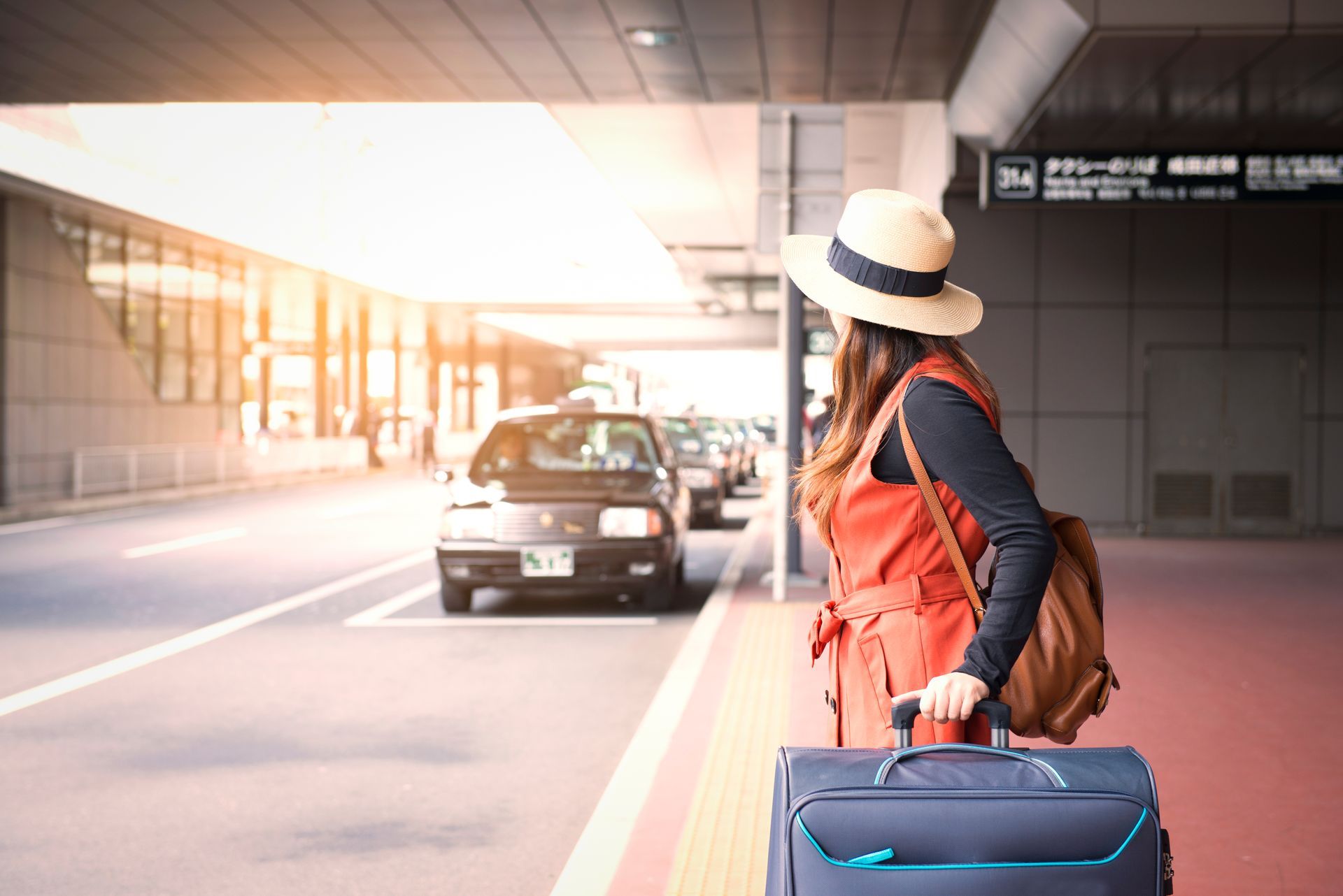 Femme coiffée d'un chapeau et portant une valise, attendant à la station de taxis.