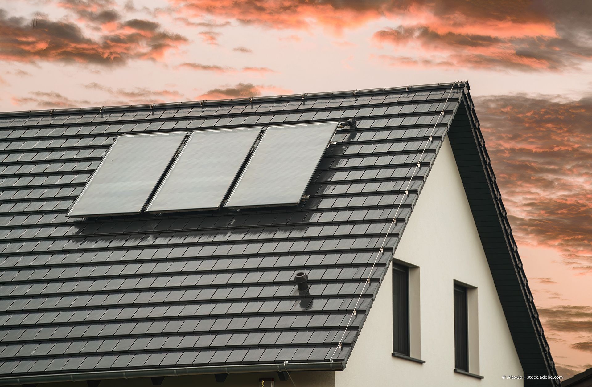 Zwei Arbeiter in Schutzausrüstung montieren Solarpaneele auf einem Metalldach.