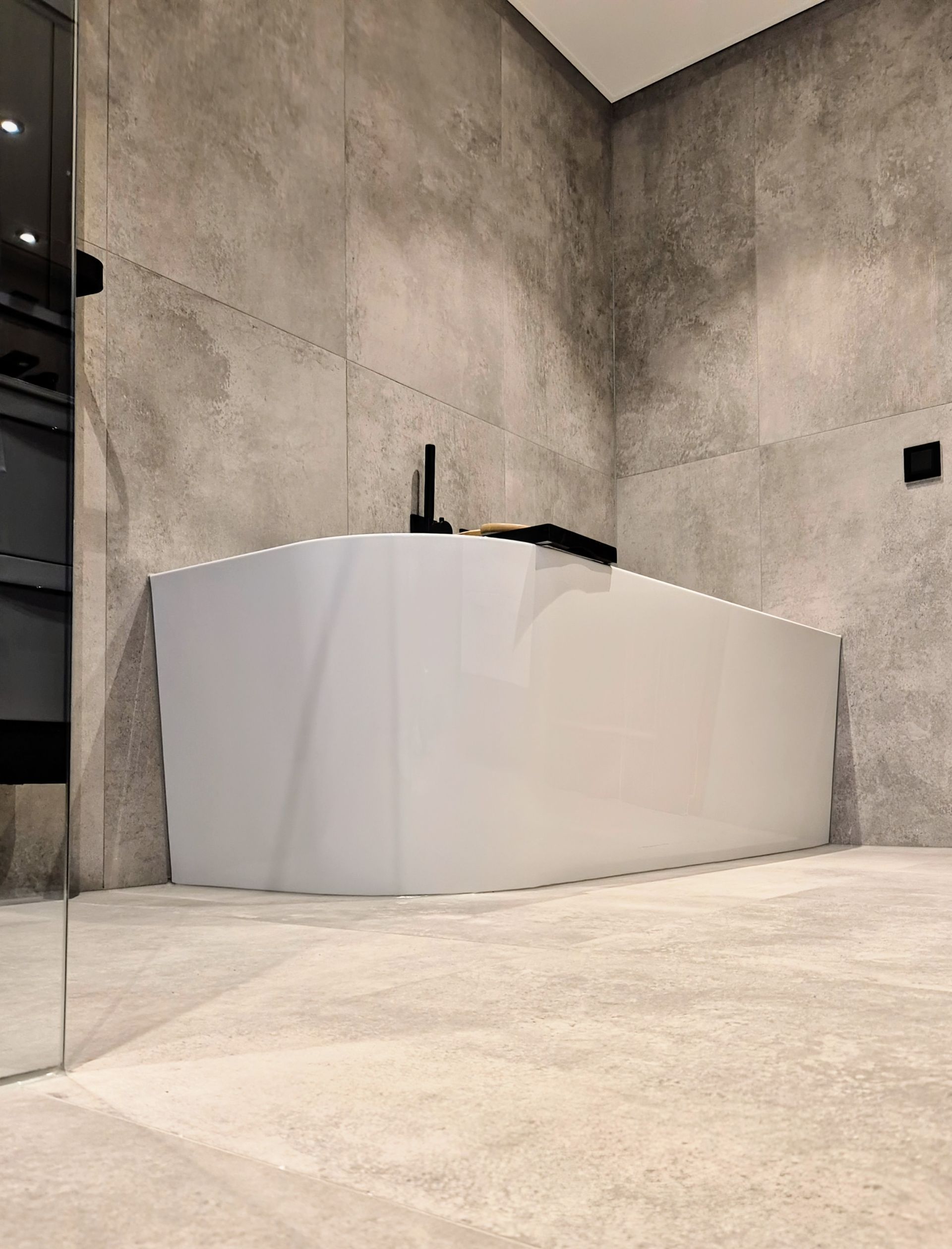 Weiße freistehende Badewanne mit klaren Linien in einer Ecke des Badezimmers, umgeben von großen, hellgrauen Fliesen an Wand und Boden.